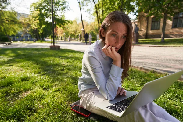 Удивлена Женщина Смотрит Экрана Ноутбука Использовании Интернета Смартфона Сидя Траве — стоковое фото