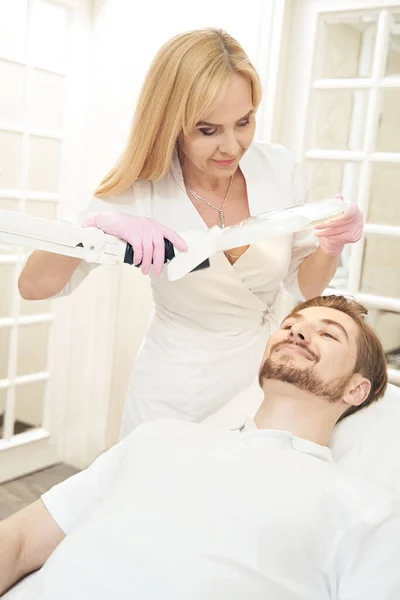 Joven Hombre Barbudo Cama Sonriendo Mientras Cosmetólogo Preparando Operación Iluminación — Foto de Stock