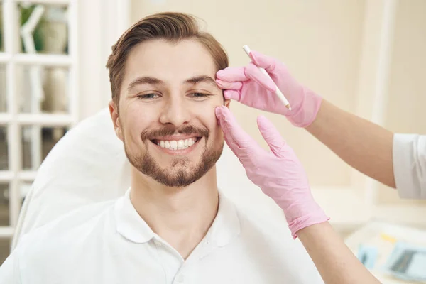 Hombre Caucásico Sonriendo Mientras Cosmetólogo Presionando Las Manos Lado Cara —  Fotos de Stock