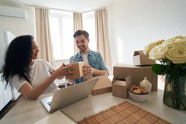 Gülümseyen internet işçileri dizüstü bilgisayarda oturmuş karton kutuyu bir arada tutuyorlar.