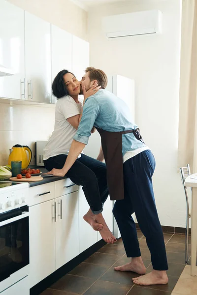 Mann Lehnt Küchentisch Und Küsst Lächelnde Glückliche Frau Auf Wange — Stockfoto