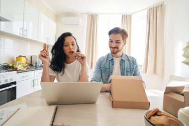 Odaklanmış kadın ve gülümseyen adam masada oturmuş dizüstü bilgisayarın ekranına bakıyor.