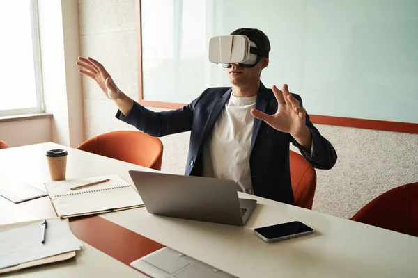 Desk worker in office in front of laptop sitting at desk and watching through augmented reality headset