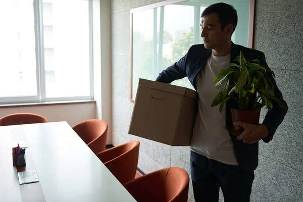 Laid off employee leaving office with box of possessions in hand and pot with plant