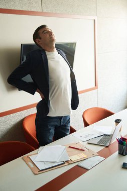 Ofis çalışanı masadaki oturma işinden kalkarken sırtını çekip kaslarını esnetiyor.