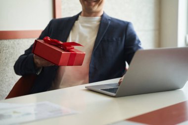 Ofisteki masadaki dizüstü bilgisayarda klavyeye tıklanırken paketlenmiş paketi elinde tutan kişi