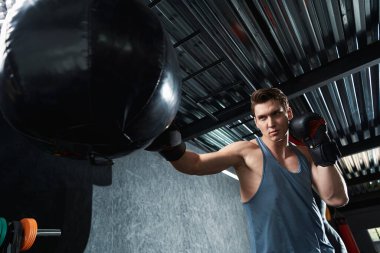 Odaklanmış boks eldivenli erkek sporcunun belden yukarı portresi kum torbasına vuruyor.