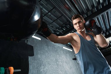 Ciddi şekilde konsantre olmuş kaslı genç sporcu antrenman sırasında kum torbasına vuruyor.