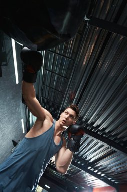 Güçlü, enerjik, genç bir boksör boks eldiveniyle kum torbasına vuruyor.