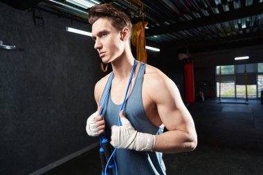 Boynunun üzerinden ip atlayan sporcunun belden yukarı portresi. Uzağa bakıyor.