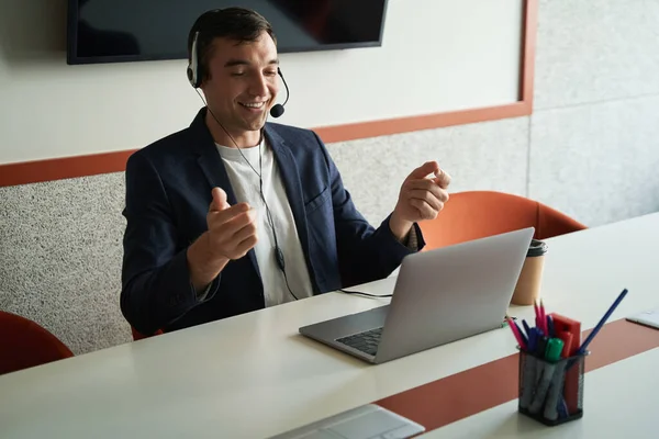 Man with headset on his head talking to another person online via laptop in office