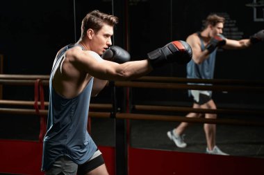 Boks eldivenli ciddi odaklı erkek sporcu sağ eliyle yumruk atıyor.