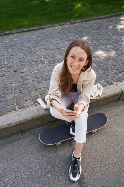 Glückliche Frau Sitzt Auf Asphalt Neben Skateboard Und Hält Smartphone — Stockfoto