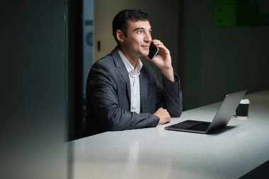 Uzun masadaki memnun Kafkas işadamı ondan önce bilgisayarla cep telefonuyla konuşuyordu.