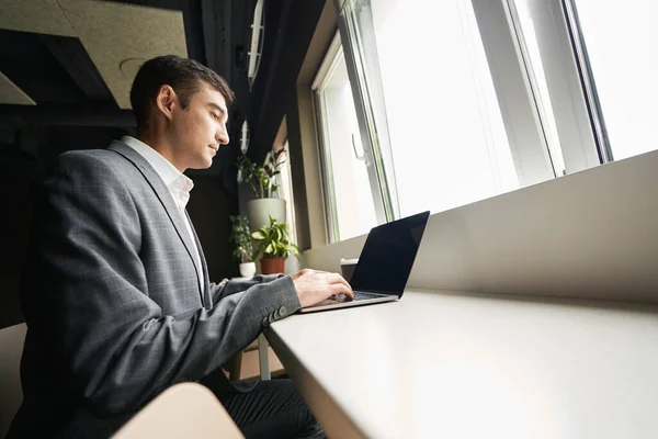 Side view of office employee working on laptop keyboard while sitting near the window