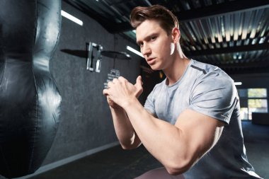 Kum torbasına vurmadan önce vücut ağırlığı egzersizi yapan kararlı formda genç bir sporcu.