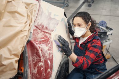 Modern benzin istasyonunda çalışan ve arabayı boyamaya hazırlayan genç bir kadın.