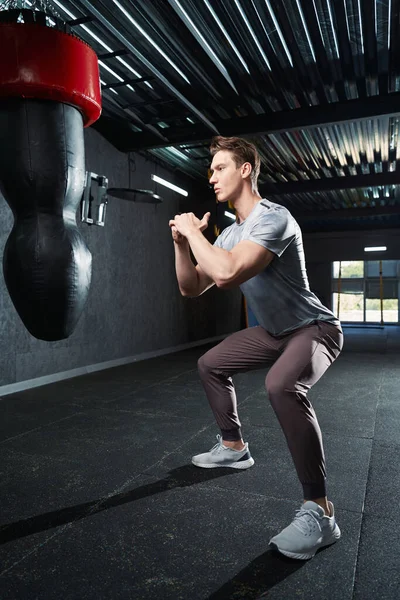 Ernsthafter Sportler Macht Kniebeugen Vor Boxsack Fitnessstudio — Stockfoto