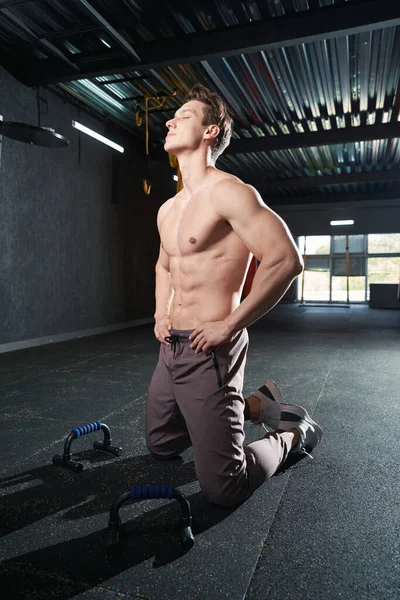 Fit young man with eyes closed kneeling on gym floor before push-up bars