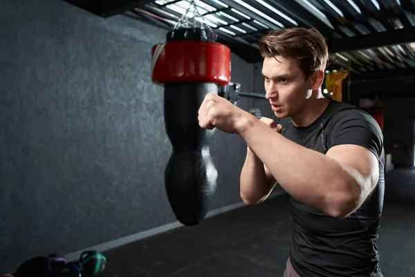 Young sportsman standing in fighting stance and throwing punches during boxing workout