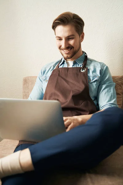Glimlachende Vrolijke Man Zittend Bank Kamer Typen Zijn Laptop — Stockfoto