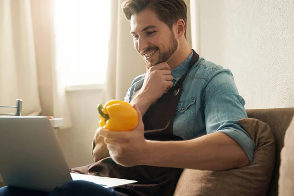 Gülümseyen Neşeli Adam Dizüstü Bilgisayarda Oturmuş Elinde Dolmalık Biber Tutuyor — Stok fotoğraf