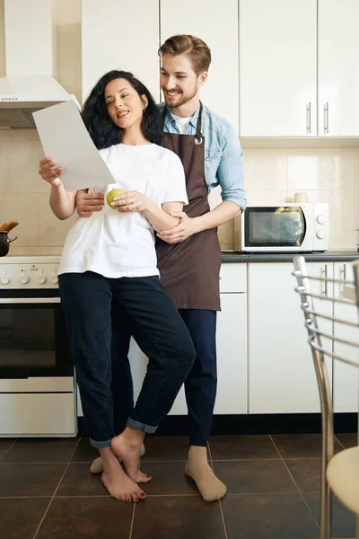 Романтичный Мужчина Обнимает Женщину Кухонным Столом Смотрит Документ Руке — стоковое фото