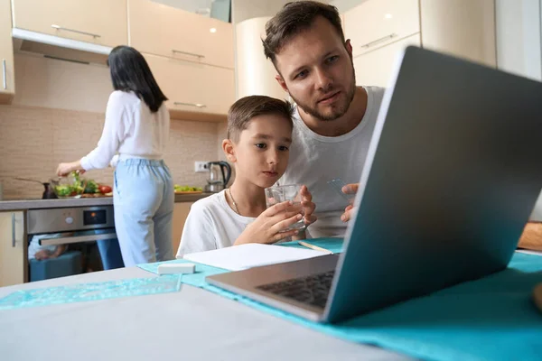 Kid Holding Glass Water Staring Laptop Screen Kitchen While Parent — 스톡 사진