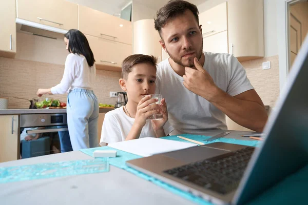 Male Parent Scratching His Chin While Studying His Son Online — 스톡 사진