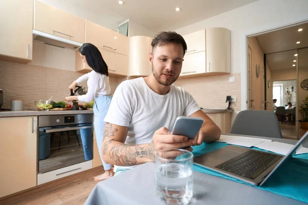 Masculino Procura Algo Telefone Celular Enquanto Sentado Antes Laptop Cozinha — Fotografia de Stock