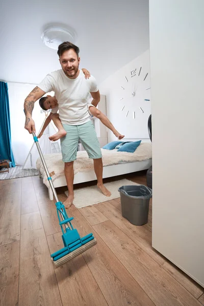 Excited Father Carrying Boy His Back Bedroom While Using Mop — Stok fotoğraf