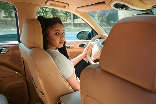 Calm young female driver sitting at steering wheel of her motor vehicle