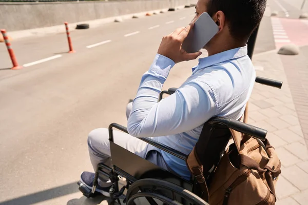 Disabled man with smartphone sitting in manual wheelchair on edge of pavement