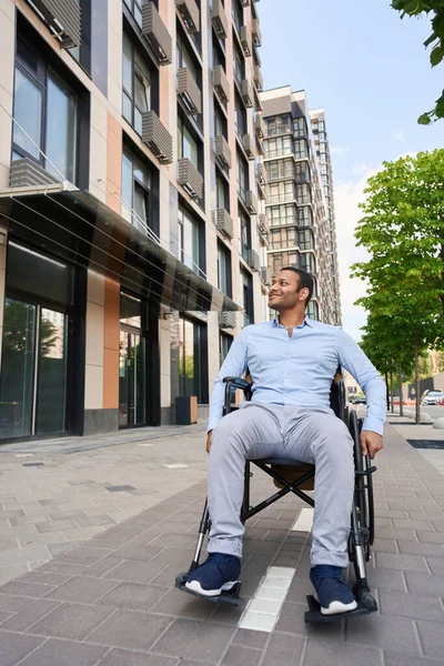 Young handicapped man riding his wheel chair and looking at office building