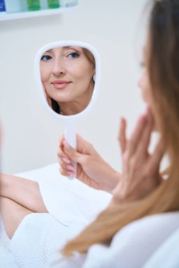 Güzellik merkezinde tedavi gören bakımlı bir kadının aynasında yansıması.