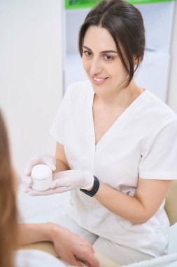 Gülümseyen güzellik uzmanı hastaya yüz bakım ürünleri hakkında danışmanlık yapıyor.