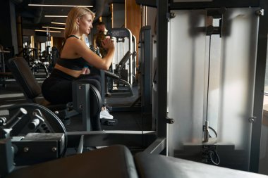 Side view of sporty woman working out on hip abduction exercise machine at gym