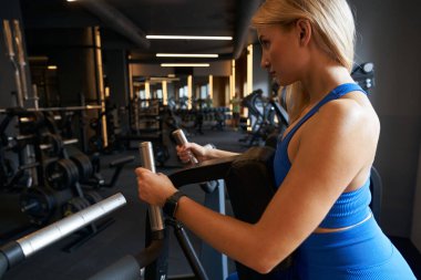 Side view of athletic female working out on strength machine in state-of-the-art gym