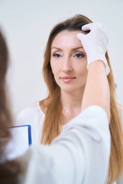 Doctor in gloves holds a medical record in his hands and examines the patient forehead
