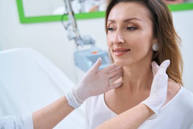 Dermatologist in gloves examining neck skin of smiling female patient