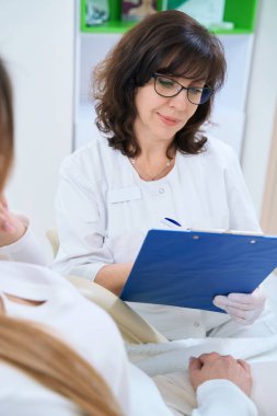 Gözlüklü esmer dermatolog hastanın tıbbi kayıtlarına şöyle yazmış: