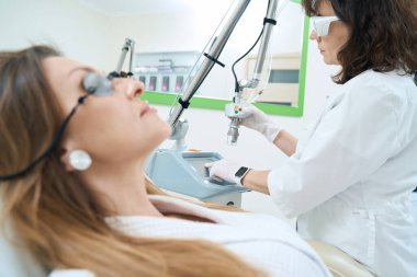 Hasta, güzellik uzmanının lazer makinesini tümörleri çıkarmak için ayarlamasını izliyor.