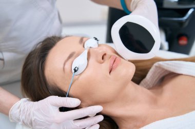 Cilt yenilenmesi için fototerapi uygulanırken koruyucu gözlük takan yetişkin bir kadın.