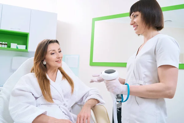 Glimlachende Schoonheidsspecialiste Die Vrouwelijke Patiënt Vertelt Huidfotorejuvenatieprocedure — Stockfoto