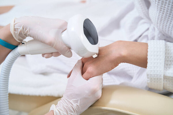 Cropped photo of doctor heals and rejuvenates the skin of the hands using phototherapy