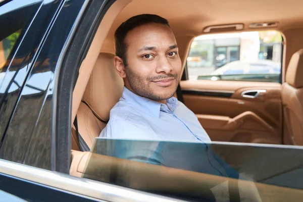 Pleased young man sitting in backseat of automobile with open window