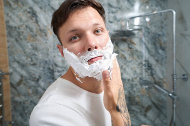 Banyoda sabah rutini, tıraş olurken bir adam köpük sürer.