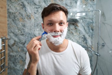 Banyoda tıraş olan neşeli genç bir adam.