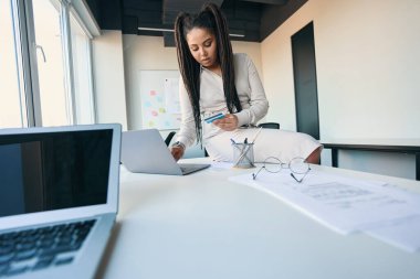 Elinde kredi kartıyla masada oturan ve dizüstü bilgisayarda yazan odaklanmış bir şirket çalışanı.