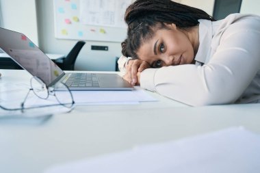 Weary young female office worker lying on desk in front of laptop